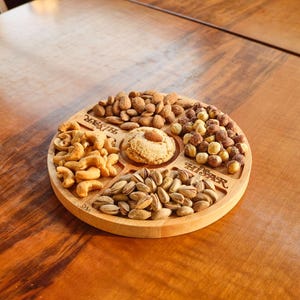 Może przedstawiać: Drewniana taca do serwowania z pięcioma sekcjami, każda wypełniona różnymi rodzajami orzechów. Taca jest oznaczona "Hi-Star" i "Snacks".