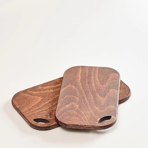 May include: Two wooden cutting boards with a brown stain. The boards have a rounded rectangular shape and a small handle cut out of the top edge.