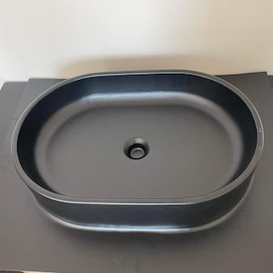 Puede incluir: Un lavabo de baño ovalado negro con un solo agujero de drenaje.
