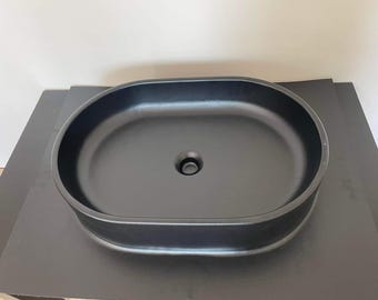 Puede incluir: Un lavabo de baño ovalado negro con un solo agujero de drenaje.