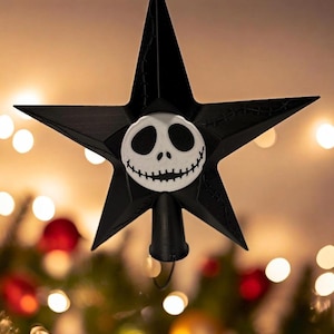 Könnte beinhalten: Schwarzer sternförmiger Weihnachtsbaumaufsatz mit einem weißen Jack Skellington-Gesicht in der Mitte. Der Stern hat genähte Details und einen schwarzen Sockel. Festliche Weihnachtsdekoration.