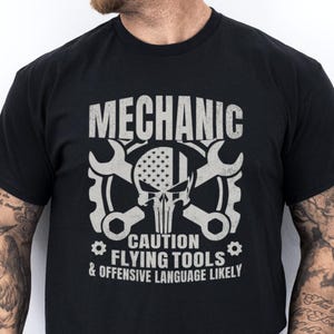 May include: Black t-shirt with a white graphic of a skull with crossed wrenches and the text "Mechanic Caution Flying Tools & Offensive Language Likely".