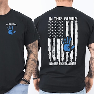 May include: A black t-shirt featuring a small blue handprint and the text NO BULLYING on the front. The back displays a large distressed white American flag graphic with a blue handprint, and the text IN THIS FAMILY, BE KIND- NO BULLYING, NO ONE FIGHTS ALONE.