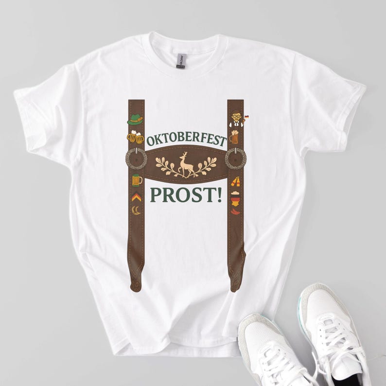 White cotton t-shirt with a printed lederhosen suspender design featuring festive Oktoberfest icons like beer mugs, pretzels, sausages, and a central deer graphic. The shirt displays the words "Oktoberfest" and "Prost!" in green text on the chest.