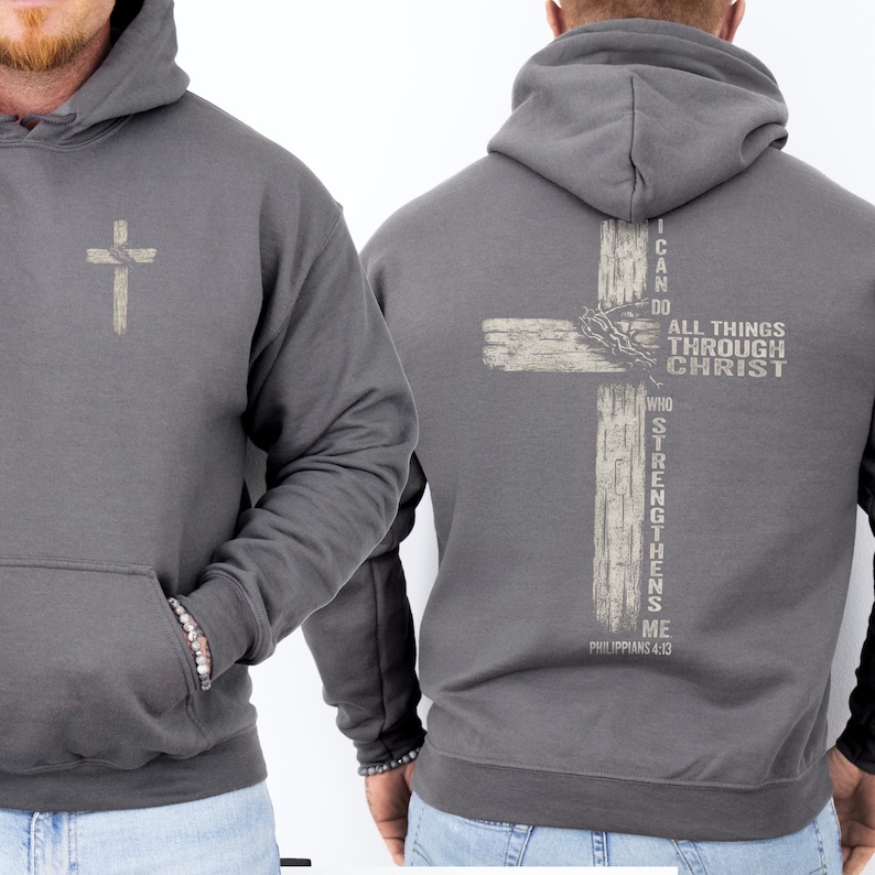 K&ouml;nnte beinhalten: Grauer Kapuzenpullover mit Fronttasche und Kordelzugkapuze. Auf der Vorderseite befindet sich ein kleines, helles Kreuz. Auf der R&uuml;ckseite ist ein gr&ouml;&szlig;eres Kreuzdesign mit dem Text "I CAN DO ALL THINGS THROUGH CHRIST WHO STRENGTHENS ME" und "PHILIPPIANS 4:13" abgebildet.