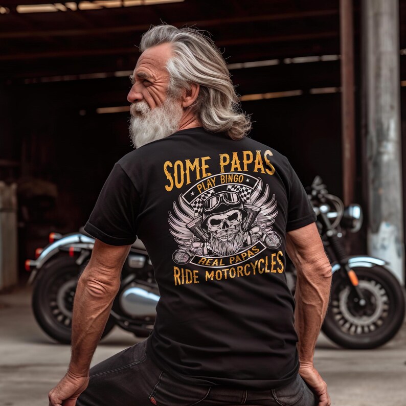 Puede incluir: Camiseta negra con un gr&aacute;fico dorado de una calavera con barba y alas. El texto "Some Papas Play Bingo Real Papas Ride Motorcycles" est&aacute; impreso en dorado en la camiseta.