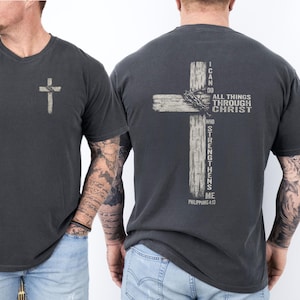 Peut inclure: T-shirt gris foncé avec une croix imprimée à l'avant et à l'arrière. Le dos présente une grande croix vieillie avec le texte "Je peux tout par celui qui me fortifie" et Philippiens 4:13.