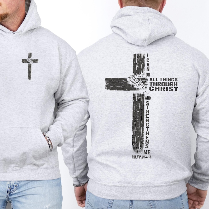 K&ouml;nnte beinhalten: Hellgrauer Kapuzenpullover mit einem schwarzen Kreuz-Grafik auf der Vorder- und R&uuml;ckseite. Auf der R&uuml;ckseite befindet sich ein gr&ouml;&szlig;eres Kreuz-Design mit dem Text "I CAN DO ALL THINGS THROUGH CHRIST WHO STRENGTHENS ME" und Philipper 4:13.