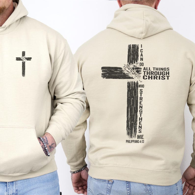 K&ouml;nnte beinhalten: Beigefarbener Kapuzenpullover mit einem schwarzen Kreuz-Grafik auf der Vorder- und R&uuml;ckseite. Auf der R&uuml;ckseite befindet sich ein gr&ouml;&szlig;eres Kreuz-Design mit dem Text "I CAN DO ALL THINGS THROUGH CHRIST WHO STRENGTHENS ME" und "PHILIPPIANS 4:13".