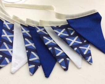 May include: A blue and white fabric bunting with a Scottish tartan pattern. The bunting is made of triangles and has a white trim.