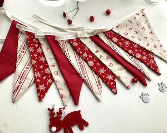 May include: A festive red and cream Christmas bunting with alternating solid red and patterned pennants. The patterned flags feature snowflakes, hearts, and other holiday designs. Decorative bells and a felt reindeer add to the holiday theme.