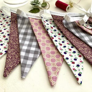 May include: A bunting banner with a variety of fabric patterns in shades of pink, white, and gray. The bunting is made of cotton fabric and has a white trim. The banner is perfect for adding a touch of whimsy to any party or event.