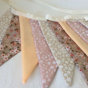 May include: A bunting banner with peach, pink, and beige fabric triangles with floral and heart patterns.
