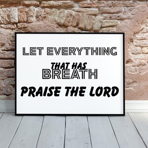 Può includere: Stampa incorniciata con le parole nere "LET EVERYTHING THAT HAS BREATH PRAISE THE LORD" su sfondo bianco. La cornice è nera, esposta contro un muro di mattoni e un pavimento in legno.