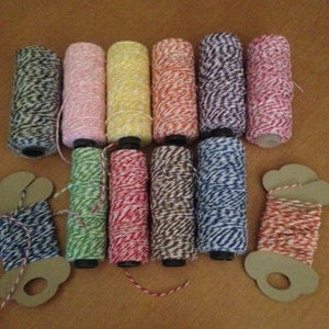 May include: A collection of colorful twine spools and rolls. The spools display a variety of colors, including pink, green, yellow, orange, and blue, with a striped pattern. The rolls are in a cloud-shaped cardboard holder.