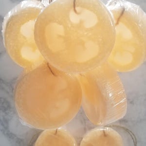 May include: Six natural loofah bath poufs hanging from twine strings. The loofahs are light brown and have a textured surface.