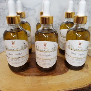 May include: Six amber glass bottles with gold lids and white droppers filled with a light brown liquid. The bottles are labeled "Abono Capilar" and "Nature". The bottles are arranged on a wooden surface.