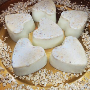 May include: Six heart-shaped soaps on a gold plate with a sprinkle of oats. The soaps are white with a subtle oatmeal texture.