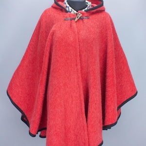 May include: A vibrant red hooded cape with black trim. The cape features a toggle closure and is displayed on a mannequin. The hood is lined with black fabric and the cape is made of a textured material.