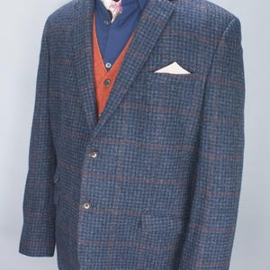 Puede incluir: Un blazer azul marino con un patrón de cuadros, combinado con una camisa azul, un chaleco naranja y un pañuelo de bolsillo estampado. El blazer tiene un diseño clásico con cierre de dos botones. También se incluye el texto "NO IMPORT DUTIES FOR U.S. BUYERS".