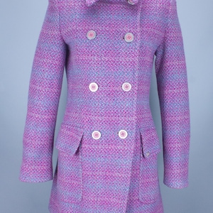 Op de afbeelding: Een dubbelrijdige roze en blauwe tweed jas met een kraag en zes zilveren knopen.