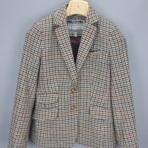 May include: A Joules brand blazer featuring a multi-colored plaid pattern in shades of tan, navy blue, and pink. The blazer has a notched lapel, two front buttons, two flap pockets, and a single chest pocket. The interior is lined with dark fabric.