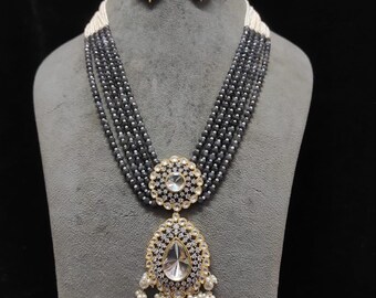 May include: A stunning jewelry set featuring a multi-strand beaded necklace with a large pendant and matching earrings. The necklace and earrings have a combination of gray beads, clear crystals, and gold-colored accents. The pendant has a large, teardrop-shaped crystal.