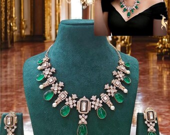 May include: A green and white diamond necklace and earrings set. The necklace features a large emerald green stone pendant with smaller emerald green stones and white diamonds. The earrings are a matching design with a smaller emerald green stone and white diamonds.