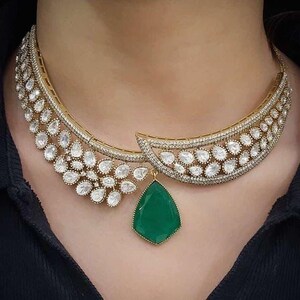 May include: A gold necklace with a large green gemstone pendant and a delicate design of small white stones.