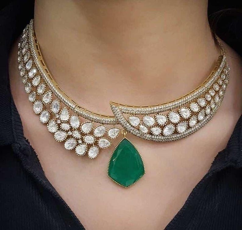 May include: A gold necklace with a large green gemstone pendant and a delicate design of small white stones.