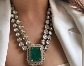 May include: A double-strand necklace featuring uncut, clear, irregular-shaped stones set in gold-toned metal. The centerpiece is a large, rectangular, deep green stone surrounded by small white stones, with a pear-shaped green stone drop pendant.