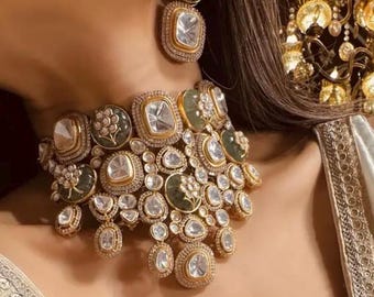 May include: A gold and silver choker necklace with large, clear, faceted stones and smaller, green stones. The necklace has a cascading design with multiple layers of stones.
