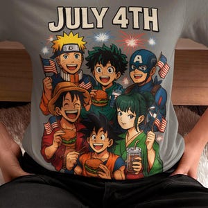 May include: Gray t-shirt with a July 4th graphic featuring cartoon characters holding American flags and burgers. The design includes fireworks and the text "JULY 4TH" in white. The shirt is a crew neck style.