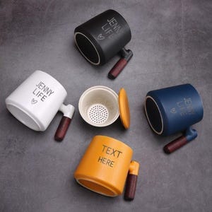 Può includere: Set di cinque tazze in ceramica con manici in legno. Quattro tazze presentano il testo "Jenny Life" con un simbolo di cuore. Una tazza presenta il testo "Text Here".