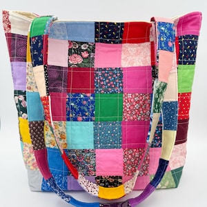 May include: A patchwork tote bag with a variety of colorful fabric squares. The bag features a mix of floral and solid patterns in pink, red, blue, green, and yellow. The straps are also made of patchwork fabric.