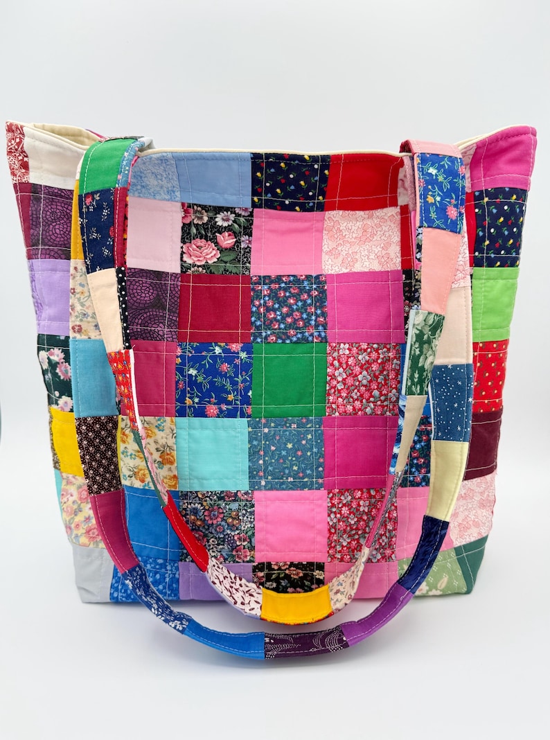 May include: A patchwork tote bag with a variety of colorful fabric squares. The bag features a mix of floral and solid patterns in pink, red, blue, green, and yellow. The straps are also made of patchwork fabric.