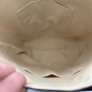 May include: Interior view of a beige tote bag with two pockets. The pockets are rectangular and sewn onto the beige fabric. The bag's interior is a light beige color, and the stitching is visible.
