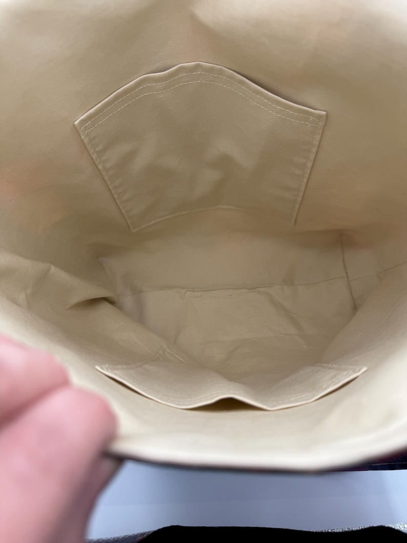 May include: Interior view of a beige tote bag with two pockets. The pockets are rectangular and sewn onto the beige fabric. The bag's interior is a light beige color, and the stitching is visible.