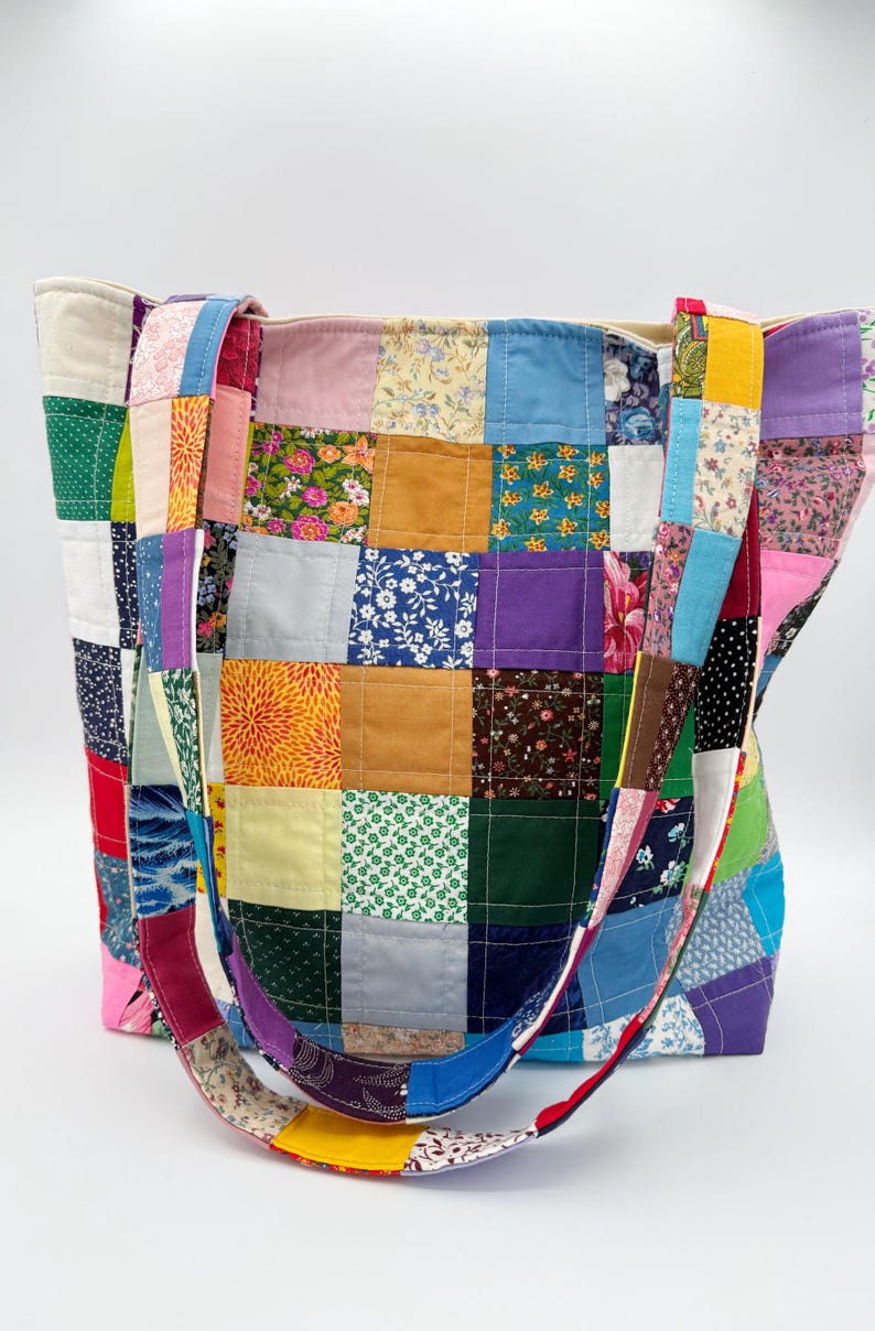 May include: A patchwork tote bag with a variety of colorful fabric squares. The bag features a mix of floral, solid, and patterned fabrics in shades of blue, pink, green, yellow, and purple. The straps are also made of patchwork fabric.