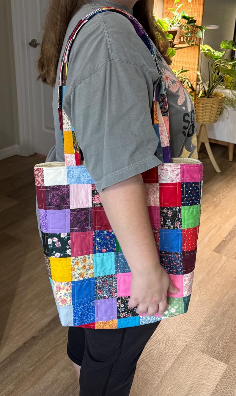 May include: A colorful patchwork tote bag with a variety of fabric squares in shades of pink, blue, yellow, and green. The bag has long straps and a rectangular shape, perfect for carrying items. The bag is handmade.