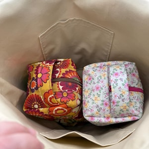 May include: Beige tote bag with two small, zippered pouches inside. One pouch has a yellow, orange, and red floral pattern. The other pouch has a light green background with a pink and yellow floral pattern. The pouches are square-shaped.