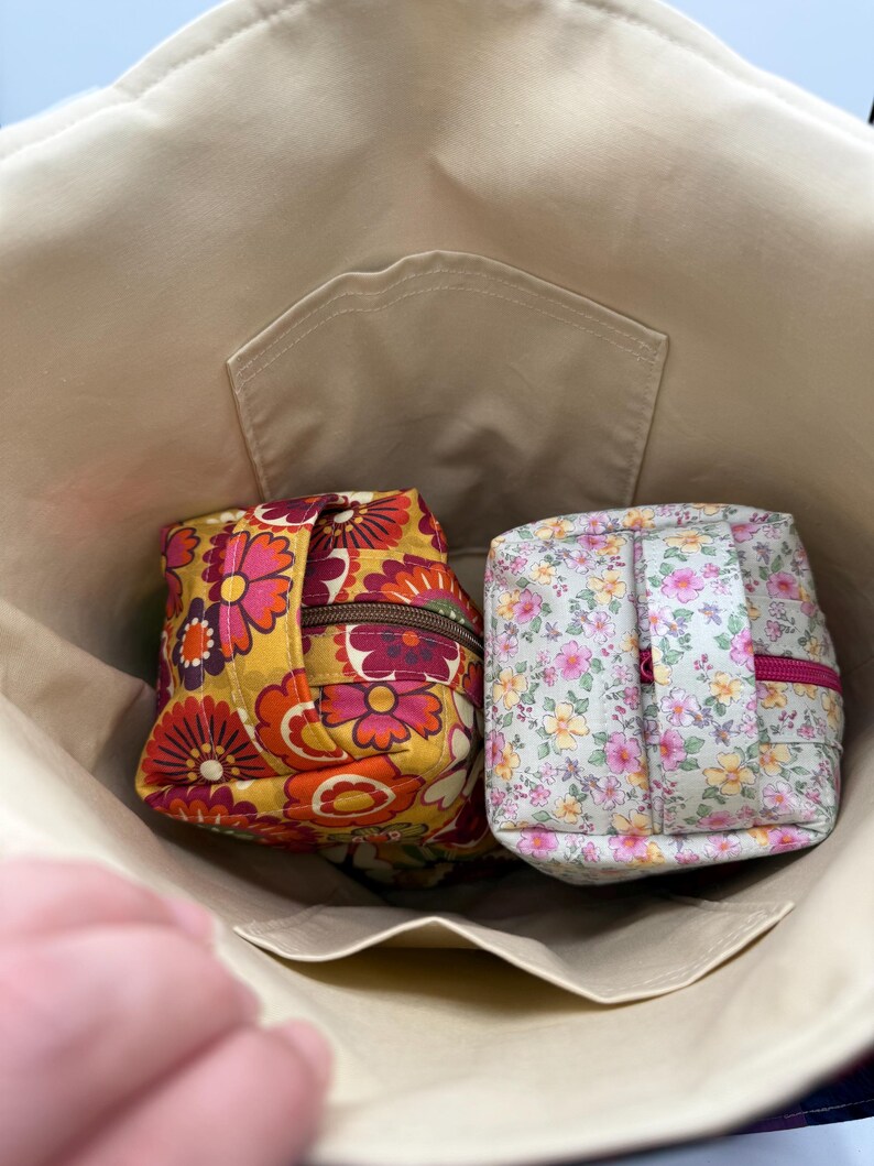 May include: Beige tote bag with two small, zippered pouches inside. One pouch has a yellow, orange, and red floral pattern. The other pouch has a light green background with a pink and yellow floral pattern. The pouches are square-shaped.