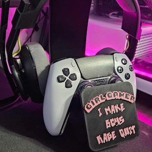 May include: A white PlayStation 5 controller with a black and pink sticker that reads "Girl Gamer I Make Boys Rage Quit".