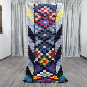 May include: A colorful Moroccan rug with a geometric pattern in shades of blue, yellow, pink, and red. The rug has a long, narrow shape and is made of wool.