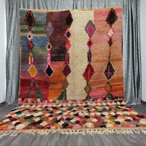May include: A colorful Moroccan rug with a geometric diamond pattern in shades of red, orange, pink, blue, and green. The rug has a fringe border and is made of wool.