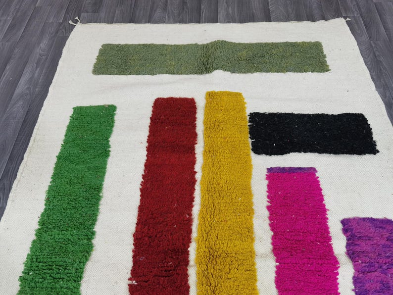 May include: A white rug with colorful stripes of green, red, yellow, pink, and purple. The stripes are woven into the rug and create a geometric pattern.