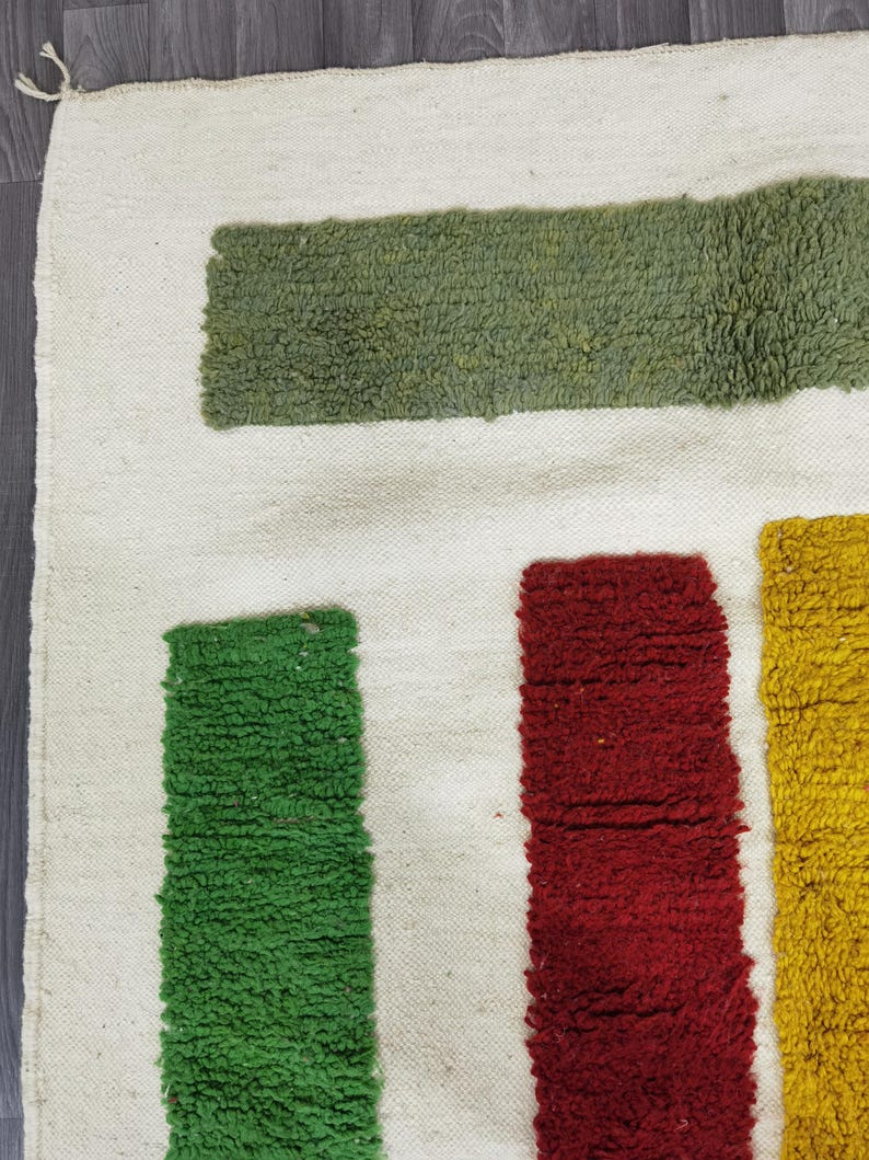 May include: A white rug with green, red, and yellow stripes. The stripes are woven into the rug and create a geometric pattern.