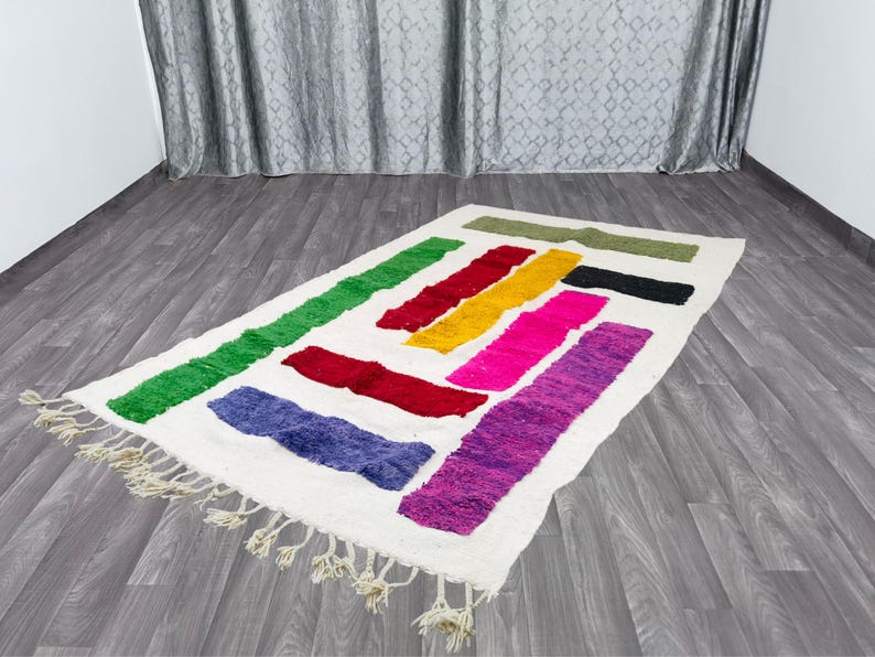 May include: A white rug with colorful stripes in shades of green, yellow, pink, purple, and red. The rug has fringe around the edges.