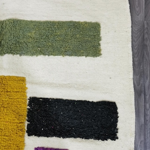 May include: A white rug with geometric shapes in green, black, yellow, and pink. The rug has a shaggy texture.