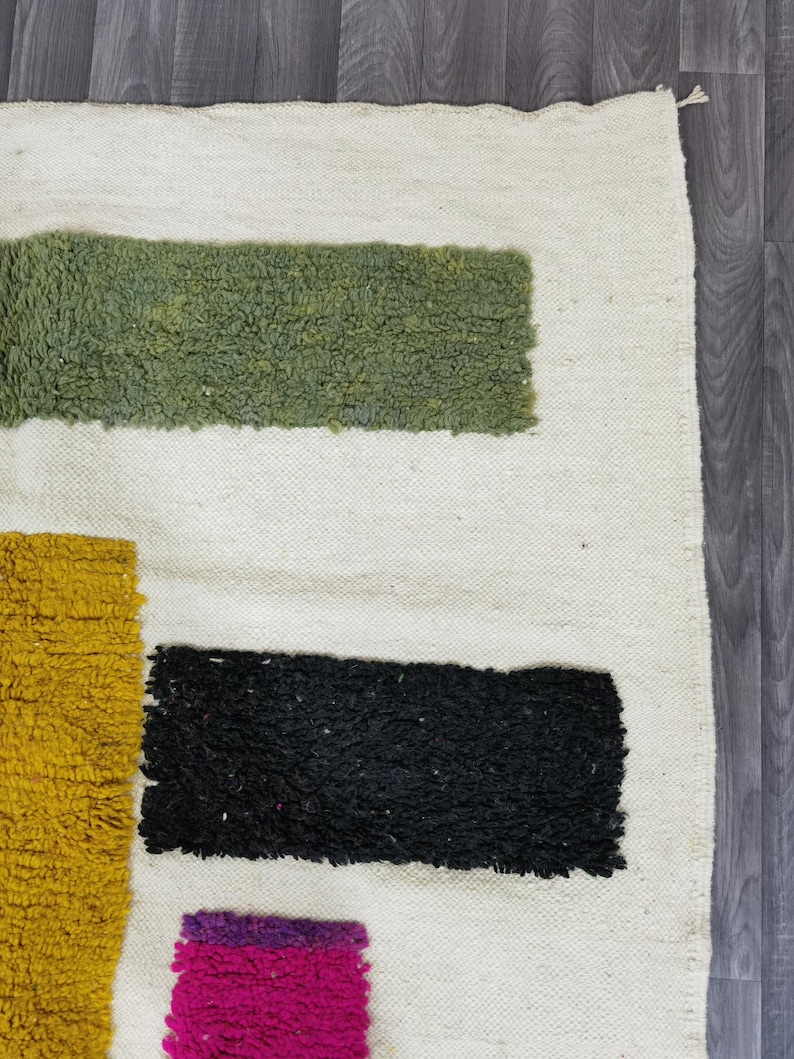 May include: A white rug with geometric shapes in green, black, yellow, and pink. The rug has a shaggy texture.